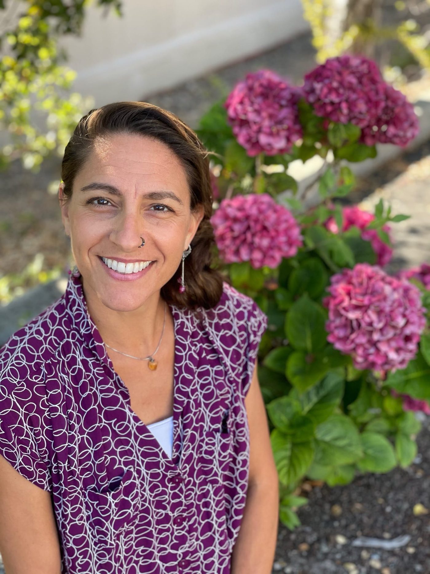 Eireann Del Bonta, RN, founder of Lotus Flow Health, smiling beside blooming hydrangeas in Santa Cruz
