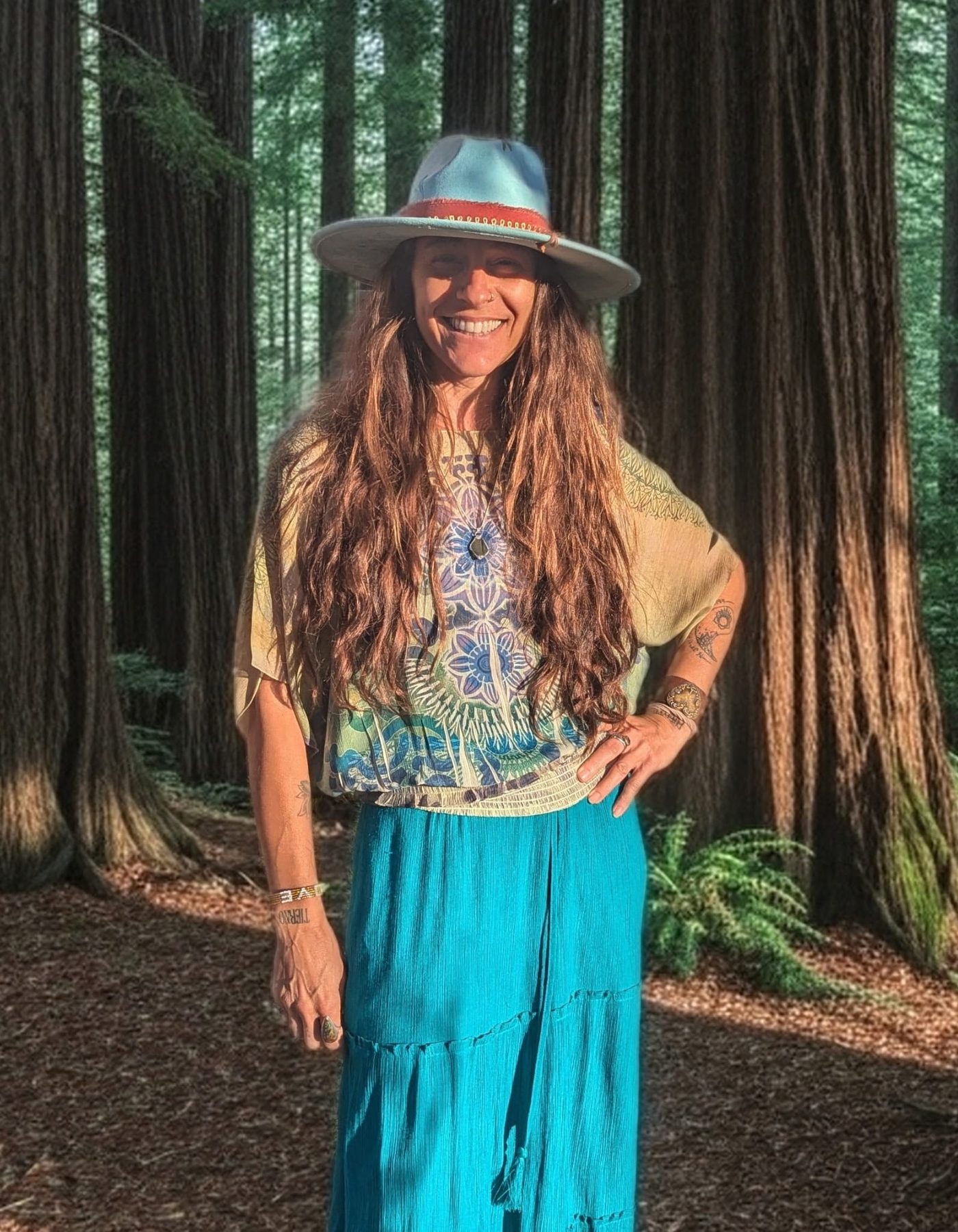 Eireann smiling in a sun hat among the redwoods